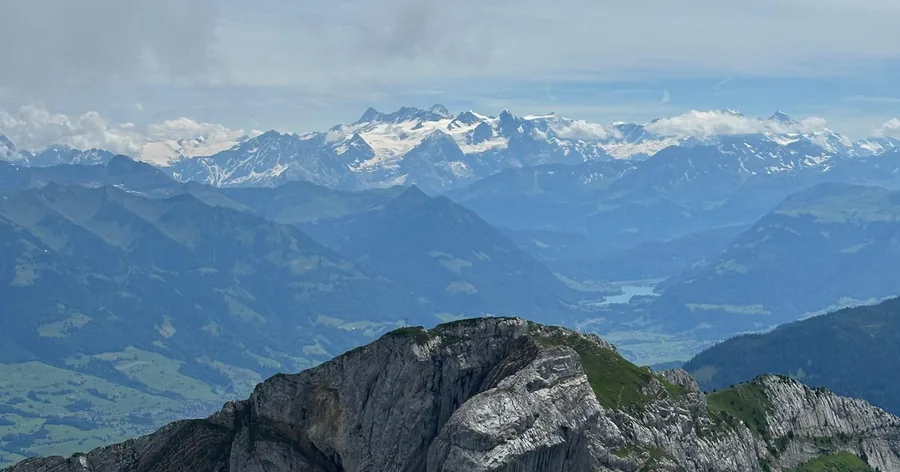 View from the summit over rocky ridges toward the snowy Alps
