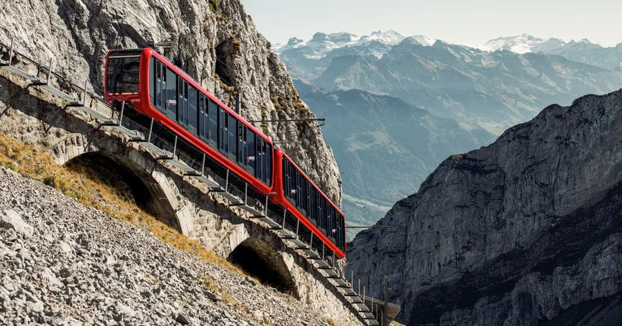 A red cog railway car on the steep track below grey limestone cliffs