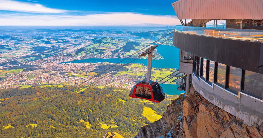 A red cableway cabin arriving at the summit building with Lucerne far below