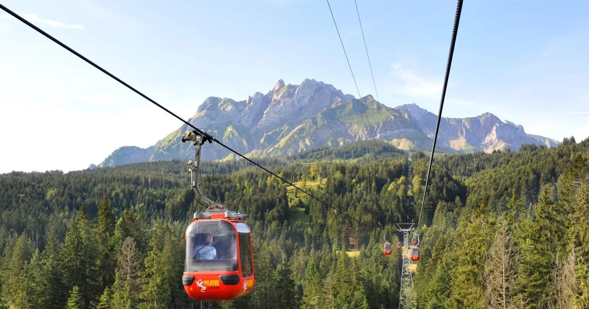 A red gondola cabin above spruce forest with the rocky Pilatus ridge behind
